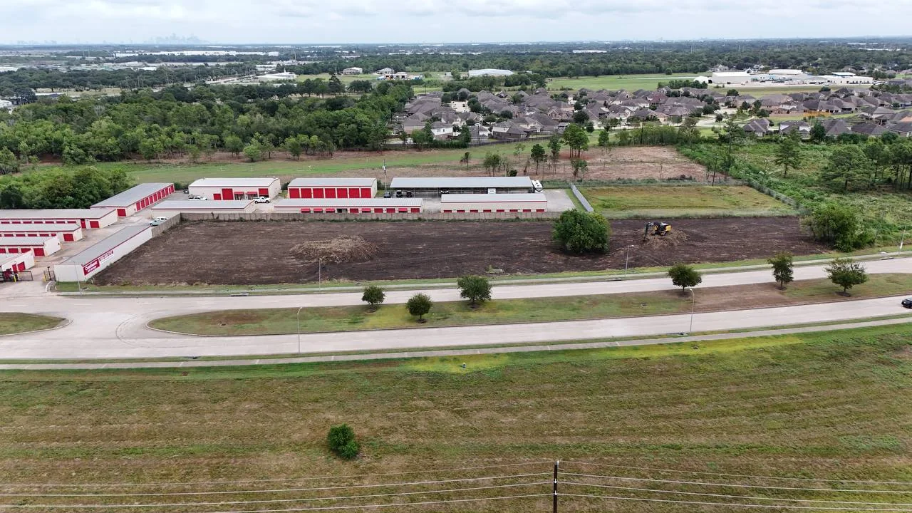 Aerial view of the McHard Flex site cleared to bare soil with a tracked machine working and cleared brush and stumps stockpiled for haul-off